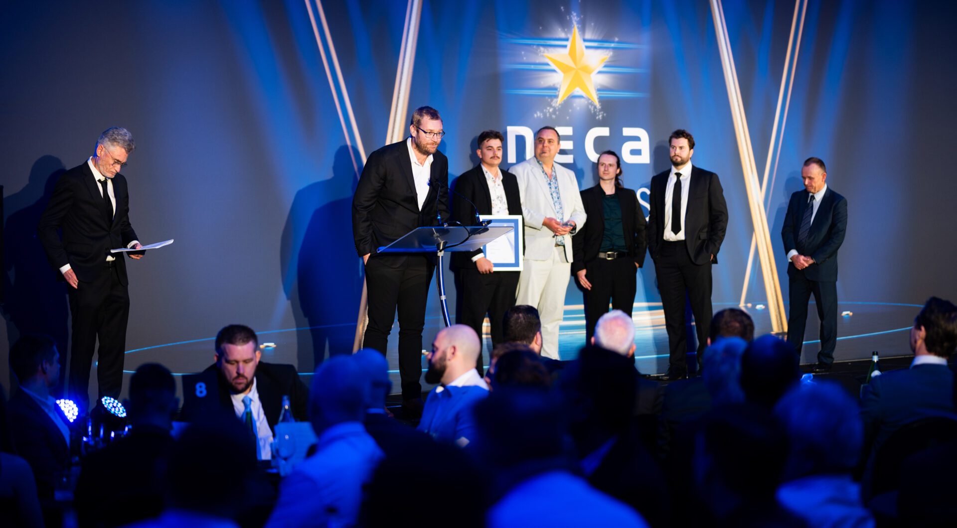 AVE Technologies team on stage giving acceptance speech at the 2025 NECA Excellence Awards after winning Small Industrial Project